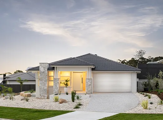 Modern single-storey residential home with white rendered and stone facade, dark roof, illuminated front entrance, white garage door, and landscaped front yard with gravel and native plants at dusk.