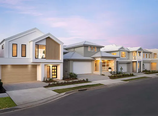Row of modern suburban townhouses with contemporary architecture, featuring white and grey facades, garage doors, illuminated windows at dusk, manicured lawns, and a paved street in Oran Park.