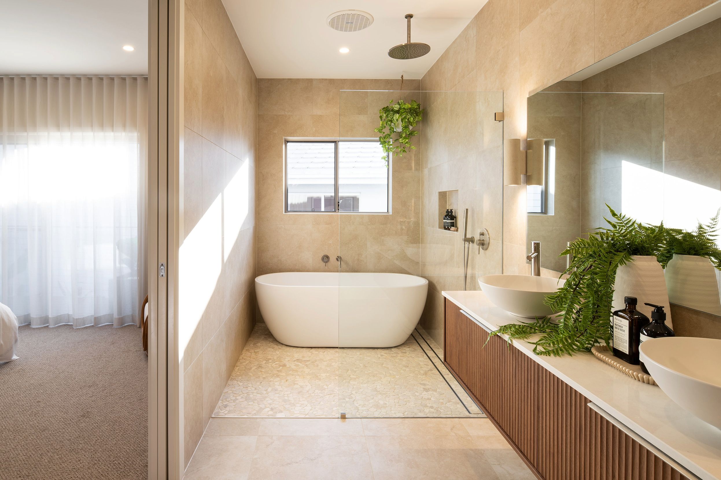 Luxury spa-style bathroom at Ridgeview resort featuring a freestanding white oval soaking tub, walk-in shower with glass enclosure, double vanity with vessel sinks, natural stone walls, indoor plants, and floor-to-ceiling windows with views.